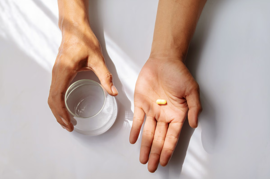 A set of hands, one of which holds a glass of water, the other, a small pill. A new non-opioid pain pill purports to be an easy, non-addictive solution to common pain, but experts advise caution.